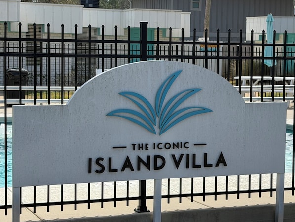 Une enseigne pour « The Iconic Island Villa », avec un logo représentant une feuille de palmier stylisée.