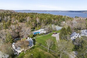 A residential area with a large house, a swimming pool, and a view of a lake. - Amore | Romantic Coastal Cottage Near Spruce Point (Boothbay Harbor)