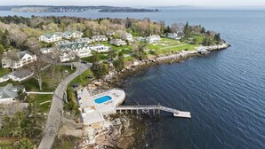 An aerial view of a coastal residential area with houses, a swimming pool, and a rocky shoreline. - Amore | Romantic Coastal Cottage Near Spruce Point (Boothbay Harbor)