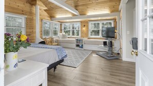 A bedroom with a bed, a window seat, a TV, and a bookshelf. - Amore | Romantic Coastal Cottage Near Spruce Point (Boothbay Harbor)