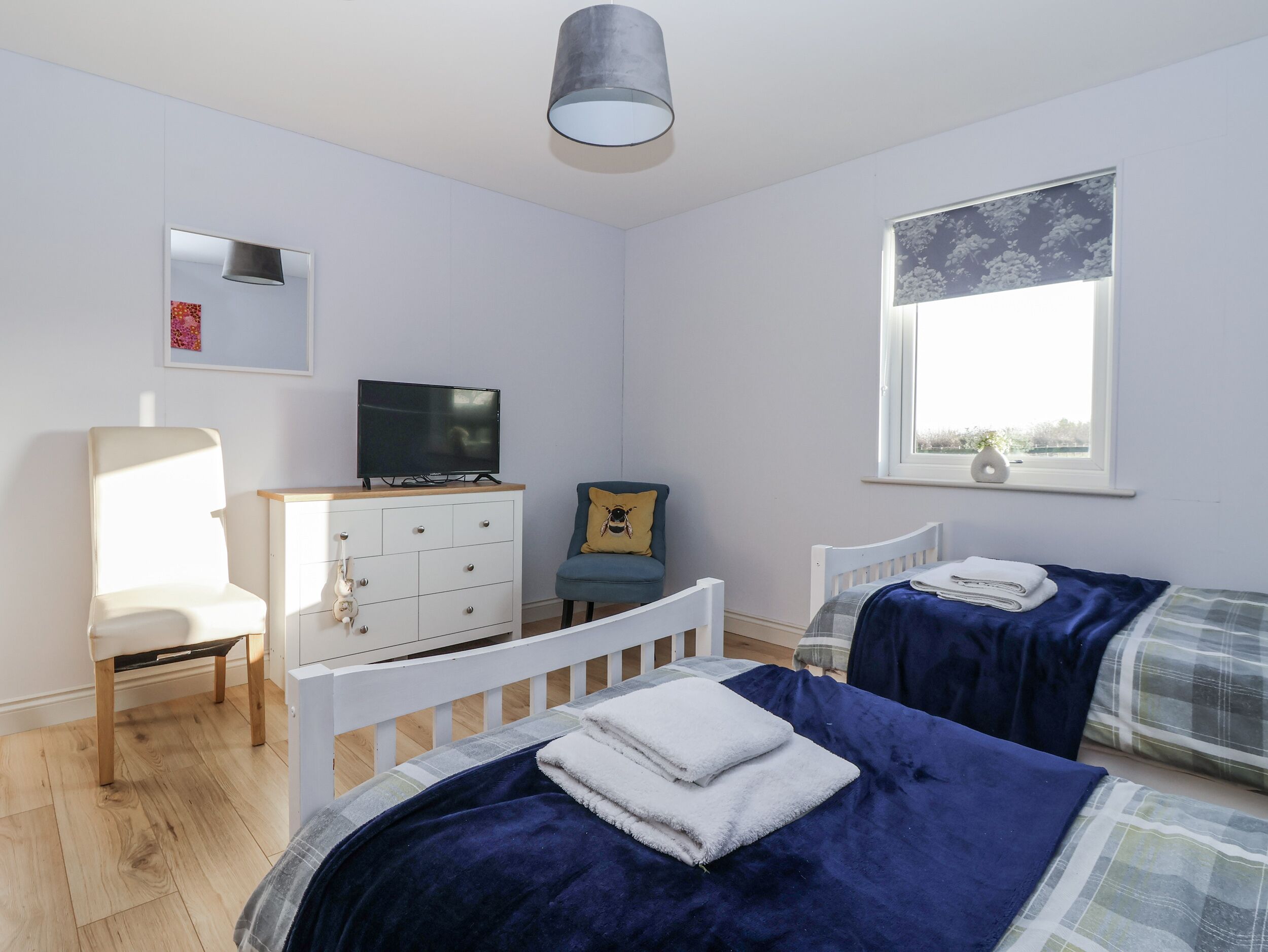 Une chambre avec deux lits, une télévision, une commode, une chaise et une fenêtre donnant sur un beau paysage.