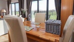A dining area with a wooden table, two chairs, a woven basket, and a view of a green landscape through large windows. - Fleetwood (Richmond)