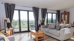 A spacious living room with a sofa, coffee table, and a view of a green landscape through large windows. - Fleetwood (Richmond)