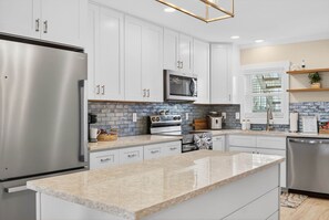 A modern kitchen with white cabinets, stainless steel appliances, a granite countertop, and a backsplash with blue and gray tiles.
