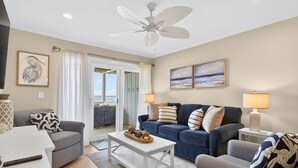 Ein Wohnzimmer mit Deckenventilator, einer Sofagarnitur, einem Couchtisch mit Dekoration und Blick ins Freie.