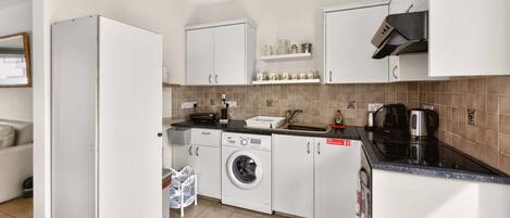 A compact kitchen with white cabinets, a washing machine, a coffee maker, and a sink.