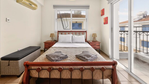 Ein Schlafzimmer mit Bett, Nachttischen, einer Bank, einem Fenster mit Aussicht und einem Balkon.