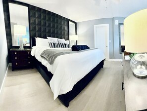 A modern hotel room with a large bed, a dark headboard, bedside tables with lamps, and a large mirror. -  The Coastal - Gulf View 8th floor condo at Bonita Springs Beach & Tennis Club (Bonita Springs)