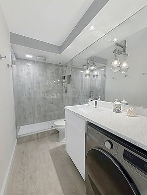 A modern bathroom with a walk-in shower, a toilet, a sink with a mirror, and a dishwasher. -  The Coastal - Gulf View 8th floor condo at Bonita Springs Beach & Tennis Club (Bonita Springs)