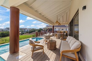Ein überdachter Außenbereich mit Pool, Holzterrasse, Korbmöbeln und Blick auf die umliegende Landschaft.