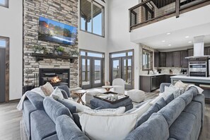 A spacious living room with a stone fireplace, large windows, and a modern kitchen. - Luxury Cabin, spectacular views, Hot Tub, Theater (Gatlinburg)
