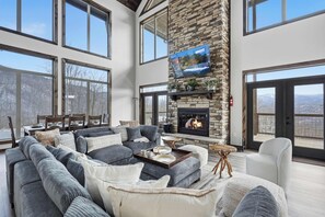 A spacious living room with a large gray sectional sofa, a fireplace, and a stone accent wall. - Luxury Cabin, spectacular views, Hot Tub, Theater (Gatlinburg)