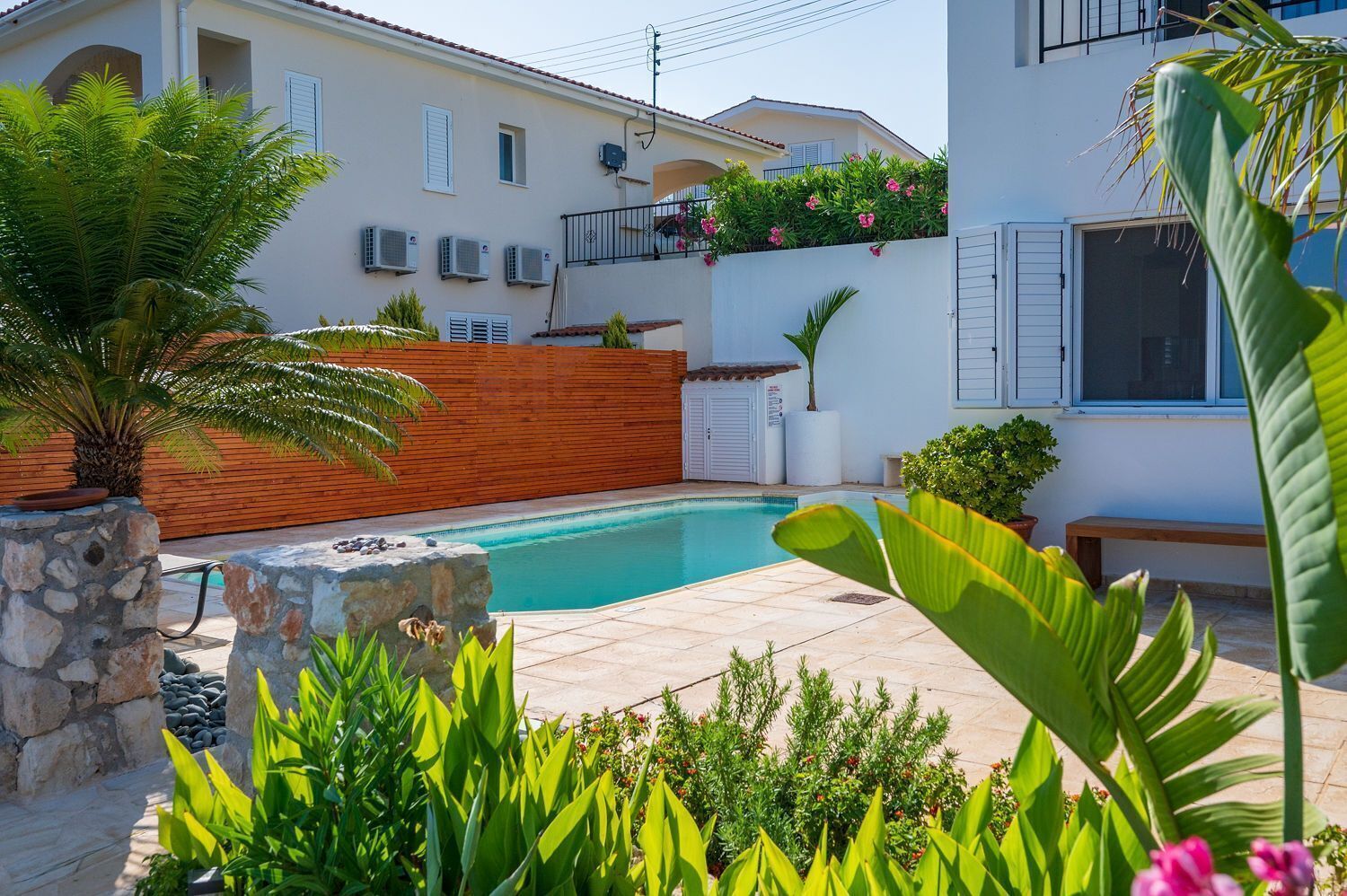 A swimming pool surrounded by a wooden fence, with a stone wall and plants in the foreground.