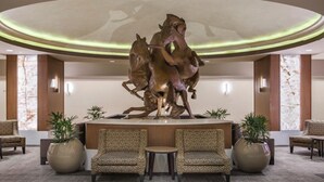 Een hal met een centrale sculptuur van een paard, twee gestreepte fauteuils en grote potplanten.