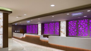 Een hotel receptie met een registratiebalie, een receptiecounter en een muur met een paars lichtpatroon.