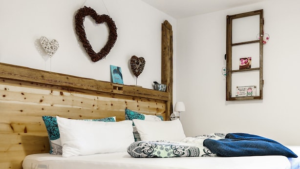 Ein Bett mit Holzkopfteil, weißer Bettwäsche und dekorativen Kissen.