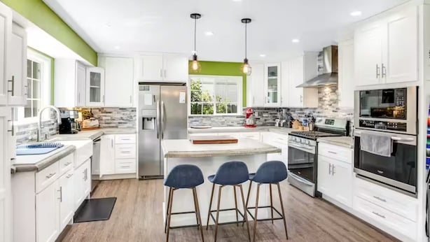 A modern kitchen with white cabinets, a central island, bar stools, a refrigerator, a stove, and a microwave.