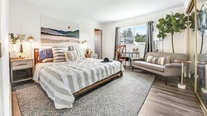 A modern bedroom with a bed, bedside tables, a sofa, and a large window.
