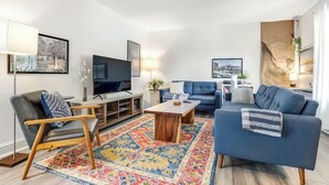 A modern living room with a flat-screen TV, a blue sofa, a wooden coffee table, and a patterned rug.