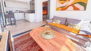 A modern living room with a wooden coffee table, a sofa with cushions, and a large abstract painting on the wall. - Ti Lodge – A Romantic Getaway with Ocean View (Cul-de-Sac)