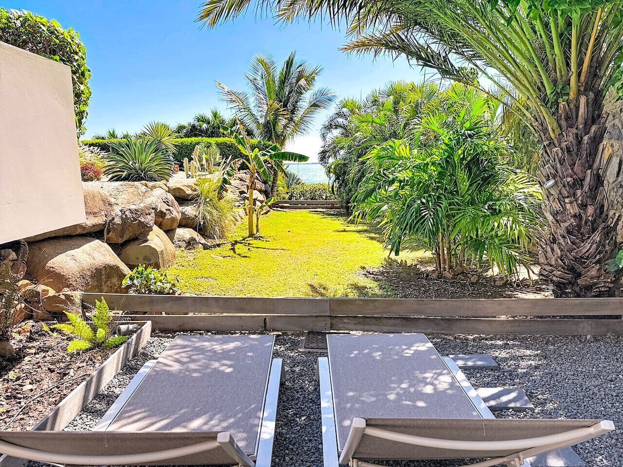 A garden view with a pathway leading to a seating area with two loungers.