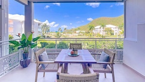 Ein Balkon mit Tisch und Stühlen, einem Blumentopf und Blick auf eine Hügelkuppe sowie Gebäude.