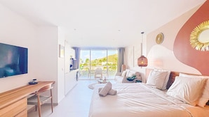 Ein modernes Hotelzimmer mit einem großen Bett, einem Schreibtisch und einem Fernseher. Es gibt einen Balkon mit Blick ins Freie.