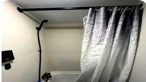 Casa de banho com cortina de chuveiro, chuveiro manual e painel de controlo na parede.
