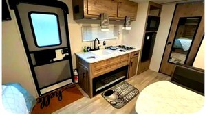 Cozinha compacta de RV com armários de madeira, pia, fogão e uma pequena geladeira.