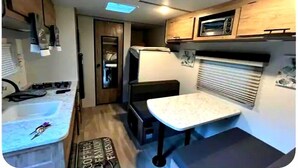 Cozinha compacta de RV com pia, fogão, micro-ondas e um pequeno espaço de jantar.