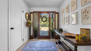 A hallway with a wooden floor, a blue patterned rug, a wooden bench, and framed botanical artwork on the wall. - Private Estate: House + Cottage, Pool & Tennis (Ojai)