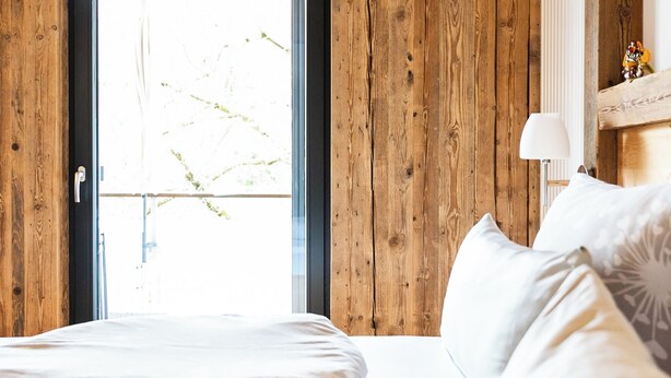 Quarto com paredes de madeira, uma janela grande e uma cama com roupa de cama branca.