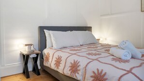 A neatly made bed with a patterned bedspread, a bedside table with a lamp, and rolled towels on the floor. - The Pilots Cottage in Apollo Bay (Apollo Bay)