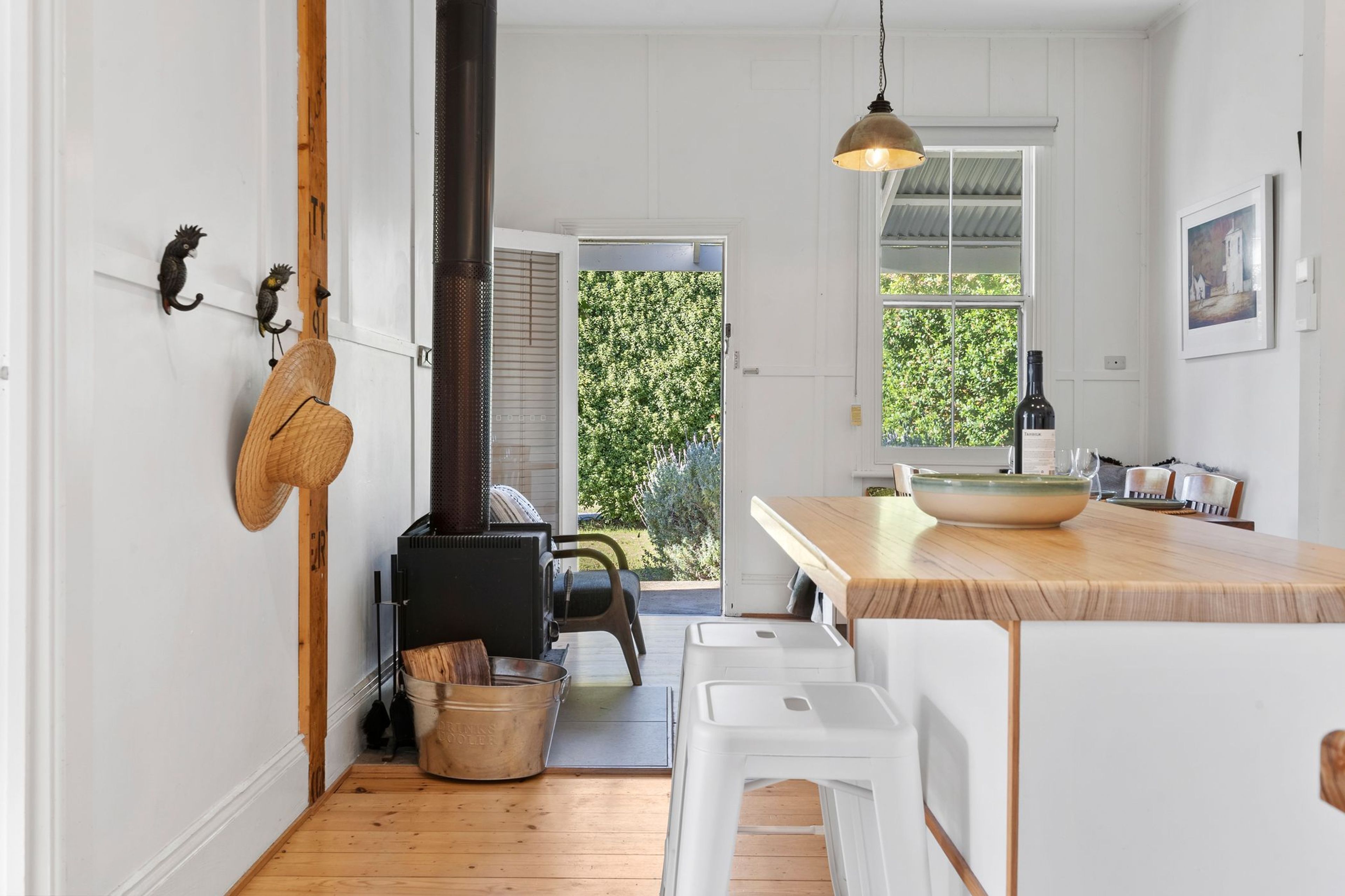 A modern kitchen with a central island, wooden flooring, and a view of a garden through the door.