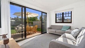 A modern living room with a grey sofa, a wooden dining table with chairs, and a large sliding glass door leading to a patio. - The Pilots Cottage in Apollo Bay (Apollo Bay)