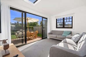 Ein modernes Wohnzimmer mit einem grauen Sofa, einem Holzesstisch mit Stühlen und einer großen Schiebeglastür, die auf eine Terrasse führt.