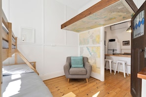 Ein Zimmer mit einem Bett, einem Sessel, einer Karte an der Wand und einer Küchenzeile.