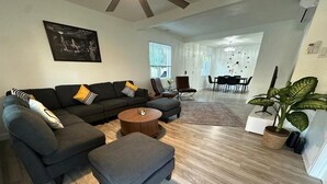 A modern living room with a sectional sofa, ottoman, and coffee table. There is a dining area with a table and chairs in the background. - Walkable to SoFi, Intuit Dome, Kia Forum World Cup (Lennox)