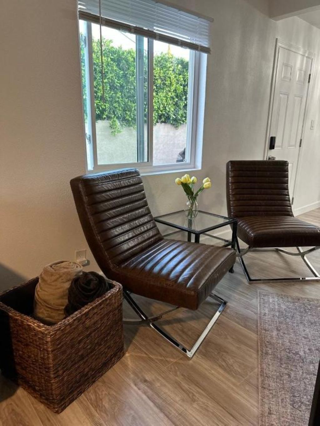 A modern living room with two brown leather chairs, a glass coffee table, and a wicker basket.