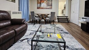 En stue med en brun lædersofa, et glasbord, et spisebord med stole, et billede på væggen og et køkkenområde i baggrunden.