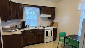 A kitchen with wooden cabinets, a stove, a sink, and a window with curtains. - Roomy 2 Bedroom Apartment 20 Minutes from Philadelphia (glenolden)