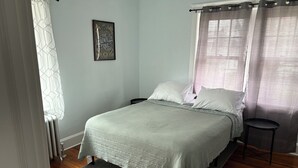 A bedroom with a bed, a nightstand, a framed picture on the wall, and a window with curtains. - Roomy 2 Bedroom Apartment 20 Minutes from Philadelphia (glenolden)