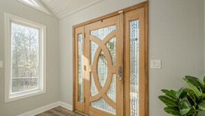 A wooden door with glass panels and a metal handle, a window with a view of trees, and a potted plant to the right. - Lakefront Luxury - Boat Slip - Kayaks - Game Room (Waleska)