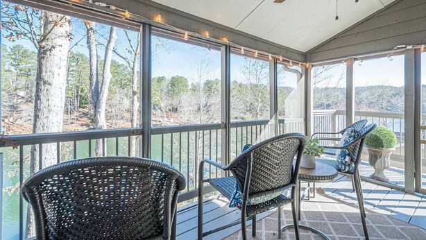 A covered outdoor area with wicker chairs and a table, large windows offering a view of trees and a body of water. - Lakefront Luxury - Boat Slip - Kayaks - Game Room (Waleska)