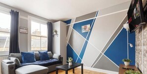 Ein modernes Wohnzimmer mit einer Couch, einem Couchtisch und einer Wand mit geometrischen Mustern.
