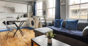 A compact living space with a kitchenette, a dining area, and a seating area with a sofa and cushions. - Relaxing 2BR Flat|Near Stores|Near Station|ST (Greater London)