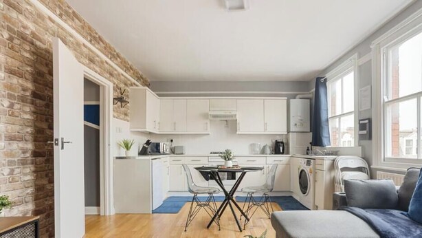 A modern kitchen with white cabinets, a dining table with chairs, and a large window.