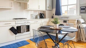 A modern kitchen with white cabinets, a gas stove, a coffee machine, and a dining area with a glass table and chairs.