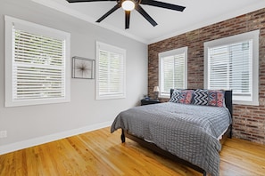Une chambre à coucher avec un lit, un ventilateur de plafond et un mur en briques.