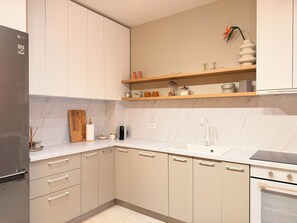 A modern kitchen with beige cabinets, a stainless steel refrigerator, a built-in oven, and a countertop with a sink and various kitchen items. - Cozy Forrest-side 2BR - Parking & Patio (Brașov)
